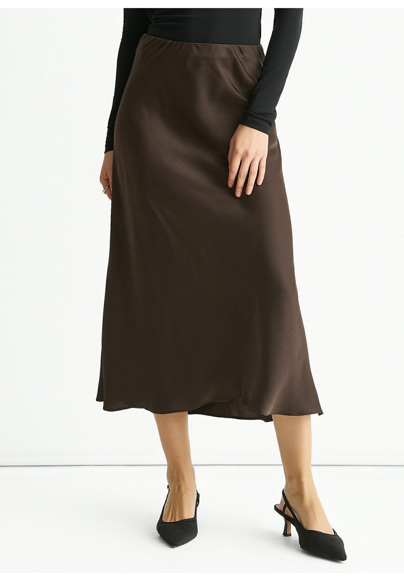 Brown satin midi skirt with a smooth texture, slight sheen, and a relaxed silhouette, paired with pointed black slingback heels.