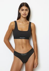 Bralette nera a coste con scollatura quadrata e banda con logo. Slip bikini neri abbinati con cintura con logo, entrambi realizzati in tessuto liscio.
