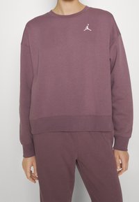 Lila sweatshirt med ribbad halsringning, utfällda axlar och logotypdetalj på bröstet. Mjuk tyg med en något boxig passform.