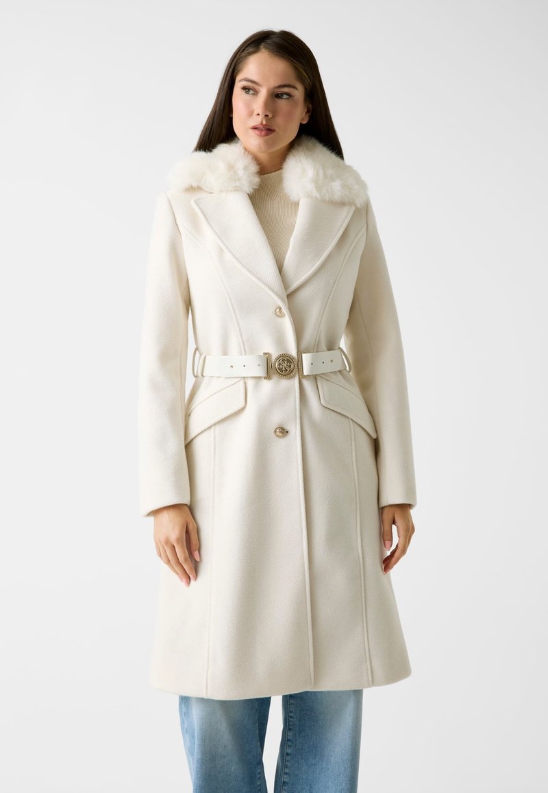 Weißer Wollmantel mit Pelzkragen, doppelter Knopfleiste, tailliertem Gürtel und zwei Fronttaschen. Glatte Textur und polierte Oberfläche.