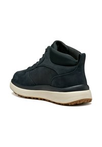 Zapatilla alta negra con cuello acolchado, suela intermedia blanca y suela rugosa marrón, mostrada desde un ángulo lateral trasero sobre fondo blanco.