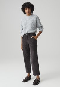 Gray fuzzy knit sweater with ribbed cuffs, paired with dark gray corduroy pants featuring side pockets. Model wears black loafers.