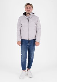 Giacca a vento grigia chiara con cappuccio nero, chiusura con zip e polsini elasticizzati. Abbinata a jeans blu e sneaker bianche.