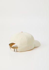 Beige színű pamut baseball sapka ívelt hajtással, hátul állítható pánttal és varrott logóval. Simább textúra, hat paneles kivitel.