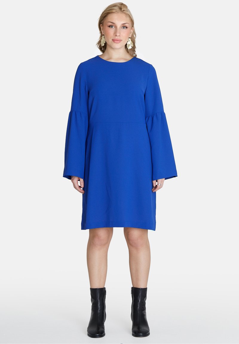 Blaues Kleid mit langen, glockenförmigen Ärmeln, rundem Ausschnitt und lockerer Passform. Getragen mit schwarzen Knöchel-Stiefeln, glattes Stoffgefühl.