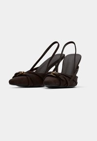 Καφέ σουέντ γόβες slingback με μυτερή μύτη, κόμπο μπροστά και χρυσό μέταλλο διακοσμητικό. Υφή με λεπτό τακούνι.