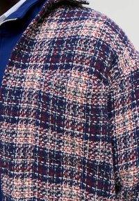 Audinio švarkas tamsiai mėlynos, raudonos ir baltos spalvų. Yra tekstūruotas langeliais raštas, minkšta medžiaga ir klasikinio tipo apykaklė.