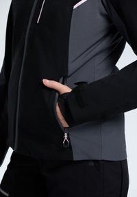 Giacca nera e grigia con chiusura frontale con zip, dettagli in zip rosa e una tasca laterale. Texture morbida con un design aderente.