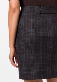 Falda de cuadros en negro y gris con una tela texturizada, que presenta un diseño ajustado y una cremallera trasera. Decorada con líneas marrones en el patrón.