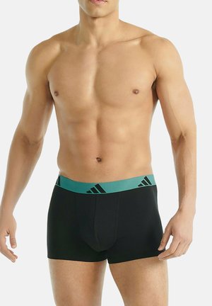 Shorts de boxe noirs avec une ceinture élastique turquoise comportant trois rayures noires et le logo Adidas. Texture de tissu lisse.