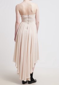 Robe sans bretelles de couleur crème avec un corsage ajusté et un ourlet asymétrique fluide. Fabriquée en tissu léger, elle comporte une fermeture éclair dissimulée à l'arrière.