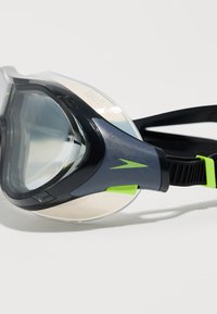 Κοντινό πλάνο μιας μαύρης και γκρι μάσκας κολύμβησης με αναπνευστήρα, με καθαρό φακό και νεον πράσινες λεπτομέρειες, που ακουμπά σε μια λευκή επιφάνεια.