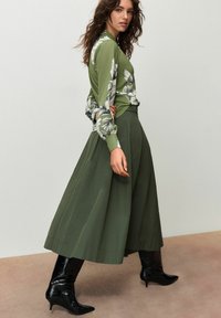 Žalia ilgomis rankovėmis palaidinė su gėlių raštu, derinama su laisvai krentančia alyvuogių žalia sijonu ir juodais aukštakulniais iki kelių. Minkšta medžiaga ir priderintas fasonas.