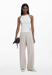 White ribbed halter top paired with light, beige striped, wide-leg pants. Model holds a brown clutch with a colorful charm.
