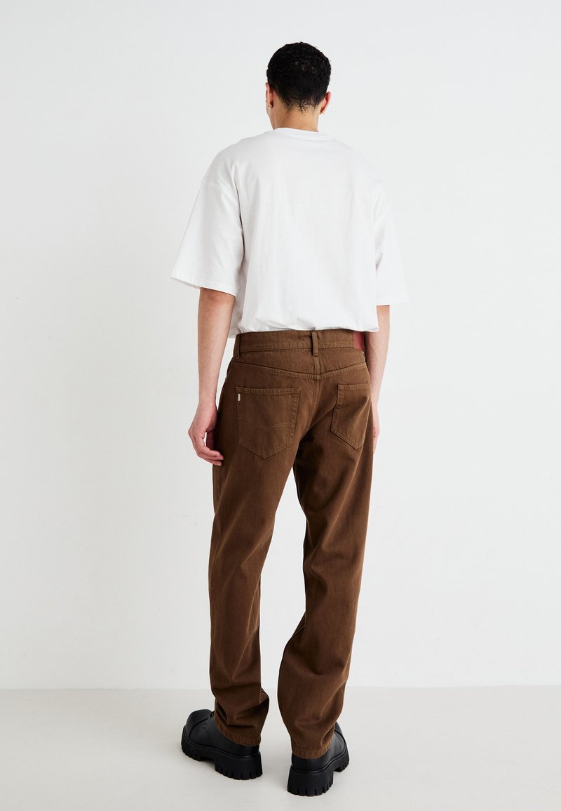 Bruine corduroy broek met een rechte snit, voorzien van twee achterzakken en een hoge tailleband, gecombineerd met een witte T-shirt met korte mouwen.