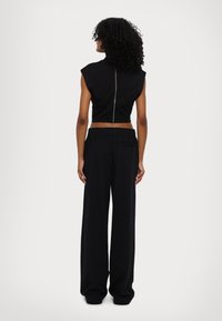 Zwarte cropped top met een hoge hals en rits aan de achterkant, gecombineerd met hoge, loszittende zwarte broeken. Zachte textuur.