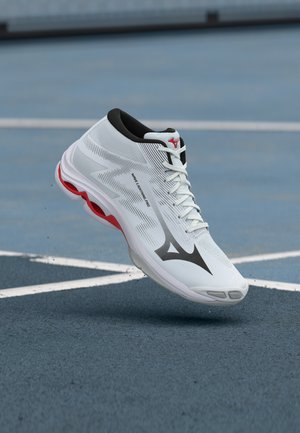 Fehér és piros sportcipő a levegőben, kék pálya felett, fehér vonalakkal, látható rajta a Mizuno logó és a "Wave Lightning Pro" felirat.