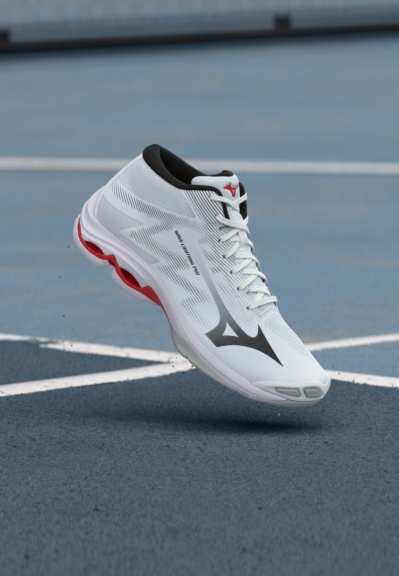 Λευκό και κόκκινο αθλητικό παπούτσι στον αέρα πάνω από μπλε γήπεδο με άσπρες γραμμές, με το λογότυπο Mizuno και το κείμενο "Wave Lightning Pro".