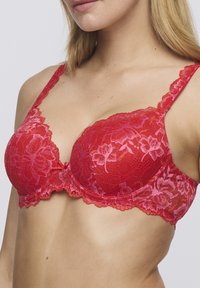 Rode kantenen beha met bloemenpatroon, voorgevormde cups, gegolfde randen en verstelbare bandjes. Heeft een strikdetail in het midden voor.
