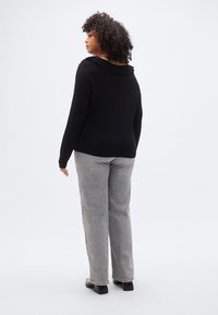 Pull noir à col à volants, associé à un pantalon large gris clair et des chaussures noires à talons blocs. Texture lisse et design décontracté.