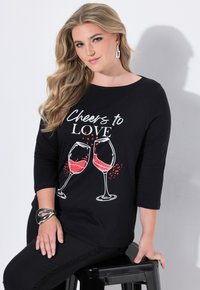 Czarna bluzka z długim rękawem z białym nadrukiem pokazującym czerwone kieliszki do wina oraz tekstem „Na zdrowie miłości”. Gładki materiał i luźny krój.