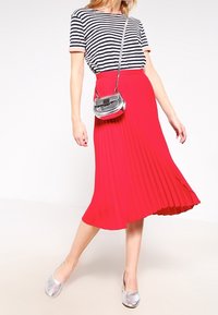 Falda midi plisada roja con una camiseta rayada en azul marino y blanco de contraste, zapatos planos metálicos plateados y un pequeño bolso cruzado plateado.
