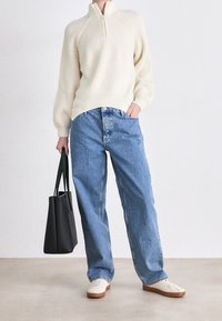 Krämfärgad ribbad stickad tröja med halvdubb, tillsammans med ljusblå högmidjade jeans. Accessoar: svart tote-väska med långa handtag.