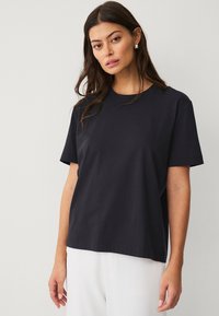 Zwarte katoenen t-shirt met korte mouwen, ronde hals en relaxte pasvorm. Beschikt over een zachte textuur en een minimalistisch ontwerp.
