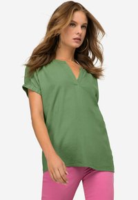 Top verde a maniche corte con scollo a V e maniche arrotolate, abbinato a pantaloni rosa. Il tessuto ha una consistenza liscia e una vestibilità comoda.