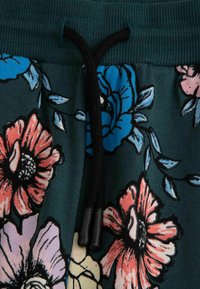 Ściągacz na ciemnozielonym materiale z dużymi niebieskimi, różowymi i czerwonymi wzorami kwiatowymi oraz czarnymi konturami.