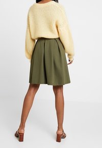 Överdimensionerad krämfärgad stickad tröja med vid halsringning, tillsammans med en plisserad olivgrön kjol och bruna blockklacksandaler.