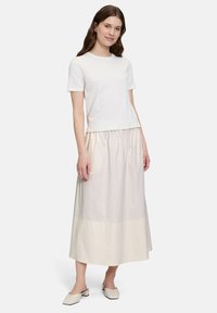 Biała krótka koszulka z rękawami, połączona z długą, jasnobeżową spódnicą z marszczonym pasem, gładkiego materiału oraz płaskim obuwiem.