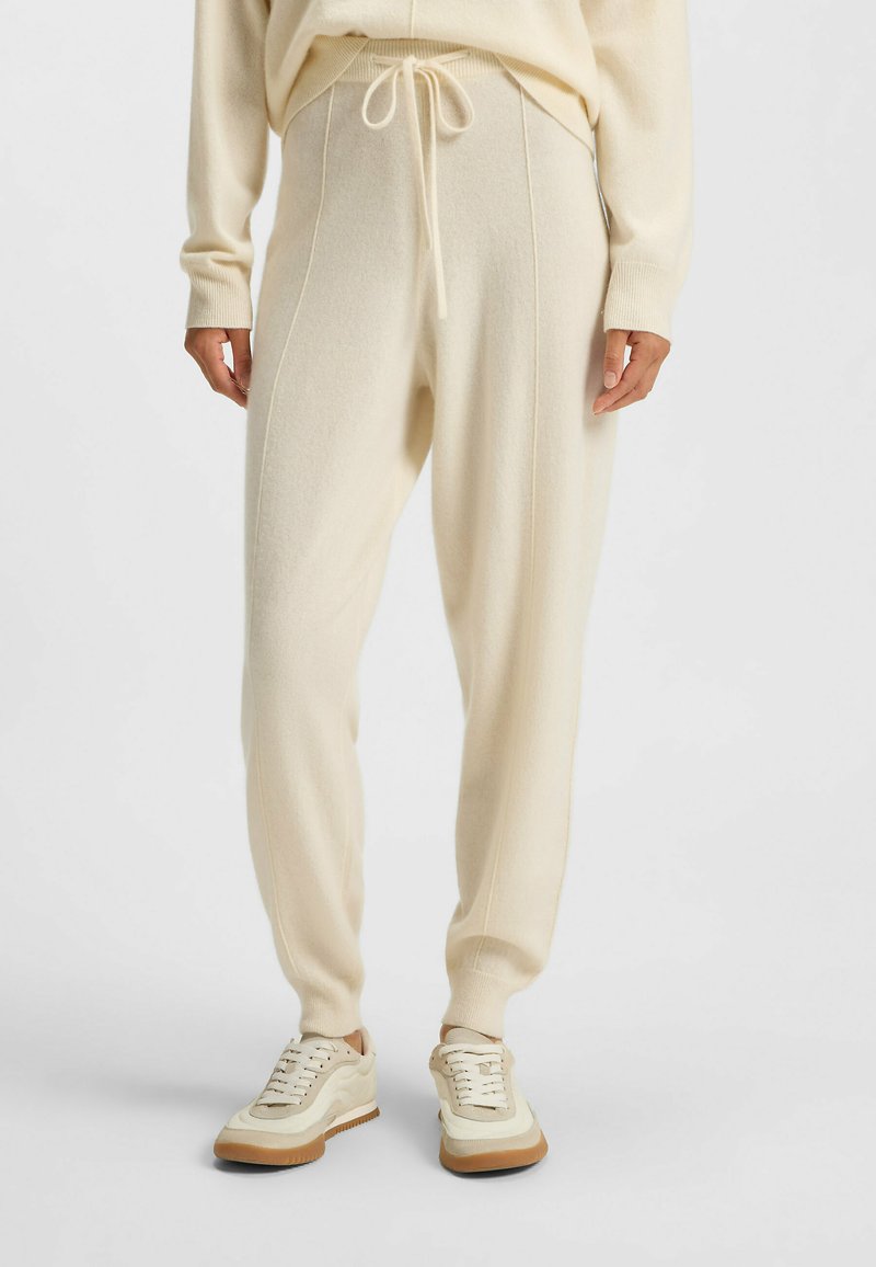 Ljusgrå joggers i mjukt material, med dragsko i midjan, sidofickor och tapered muddar, tillsammans med beiga sneakers.