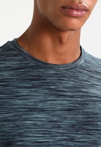 Kortärmad tröja med rund hals i ett blått och grönt melerat mönster. Tyget verkar ha en texturerad yta med en mjuk finish. Inga anmärkningsvärda detaljer eller accenter.