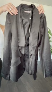 Must must-blazer, millel kaelus, üks nupuga sulgemine, pikad varrukad ja struktureeritud õlad. Silt nähtav krae sees.