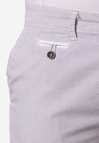 Primer plano de pantalones gris claro que muestra un pequeño bolsillo trasero abotonado y un lazo para el cinturón con tela texturizada.