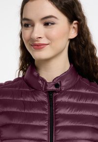 Bordowa kurtka puchowa z wysokim kołnierzem, wertykalnym, pikowanym wzorem, zapięciem na zamek oraz czarnymi guzikami zatrzaskowymi. Gładka, błyszcząca tekstura.