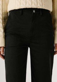 Zwarte broek van katoen met een gladde textuur. Hooggesneden ontwerp met een knoopsluiting en zijzakken.