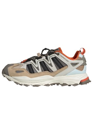 Polkujuoksukenkä, jossa on beigeä, harmaata ja mustaa materiaalia, teksturoitu päällinen, kestävä ulkopohja ja kirkkaan oranssi korostus.