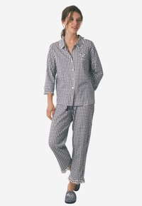 Ternet bomulds pyjamassæt bestående af en knap-åben top med lomme, lange ærmer og matchende bukser med flæsekanter. Mørkeblå og hvid mønster.