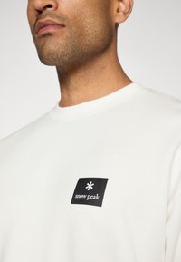 Felpa crema con un patch logo quadrato nero, testo bianco e simbolo di stella, tessuto testurizzato e scollatura a girocollo.