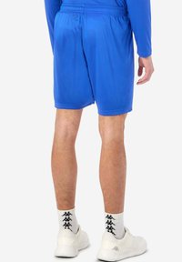 Blå idrottsshorts med elastisk midja, slät yta och en längd till mitten av låret, tillsammans med vita skor och mönstrade strumpor.