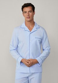 Hellblau gestreiftes Pyjama-Set mit Reverskragen, blauer Paspelierung, Brusttasche und Knopfleiste. Weicher Stoff, lange Ärmel, taillierte Passform.