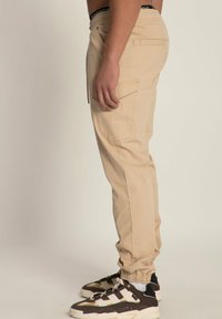 Beige cargobroek met elastische boorden, een drawstring taille en zijzakken. Heeft een zachte, katoenachtige textuur.