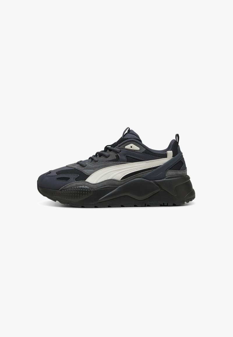 Zapatillas Puma con una parte superior de color gris oscuro, una franja lateral blanca, suela negra texturizada, paneles de malla y un diseño redondeado para mayor comodidad.