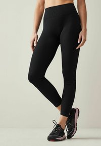 Sorte ribbede leggings med høj talje, der har en glat tekstur og tapered design, parret med sort og pink træningssko.