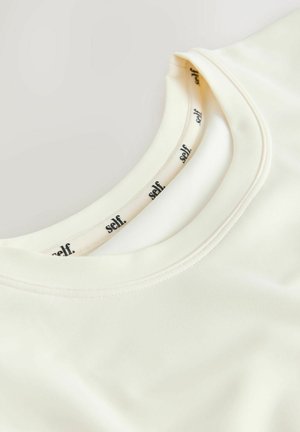Cream-colored, short-sleeve shirt with a rounded neckline. Soft fabric with smooth texture. Label reads "self" inside the collar.