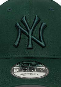 Casquette de baseball en tissu vert avec un logo "NY" noir brodé en relief, à l'arrière ajustable, et une étiquette circulaire portant la mention "9FORTY ADJUSTABLE."