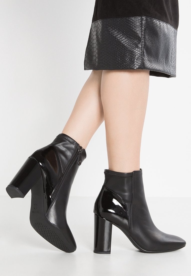 Czarne botki za kostkę z lakierowanym wykończeniem, na słupku i z bocznymi zamkami. Gładki skórzany materiał i dopasowany krój. Brak widocznych ozdób.