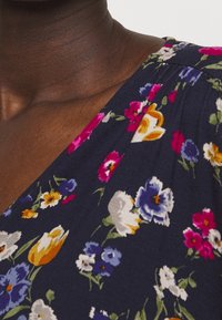 Blommig klänning i mörk marinblått tyg, med färgglada blommönster i rosa, gult och blått; mjuk textur med v-ringning och veckdetaljer.